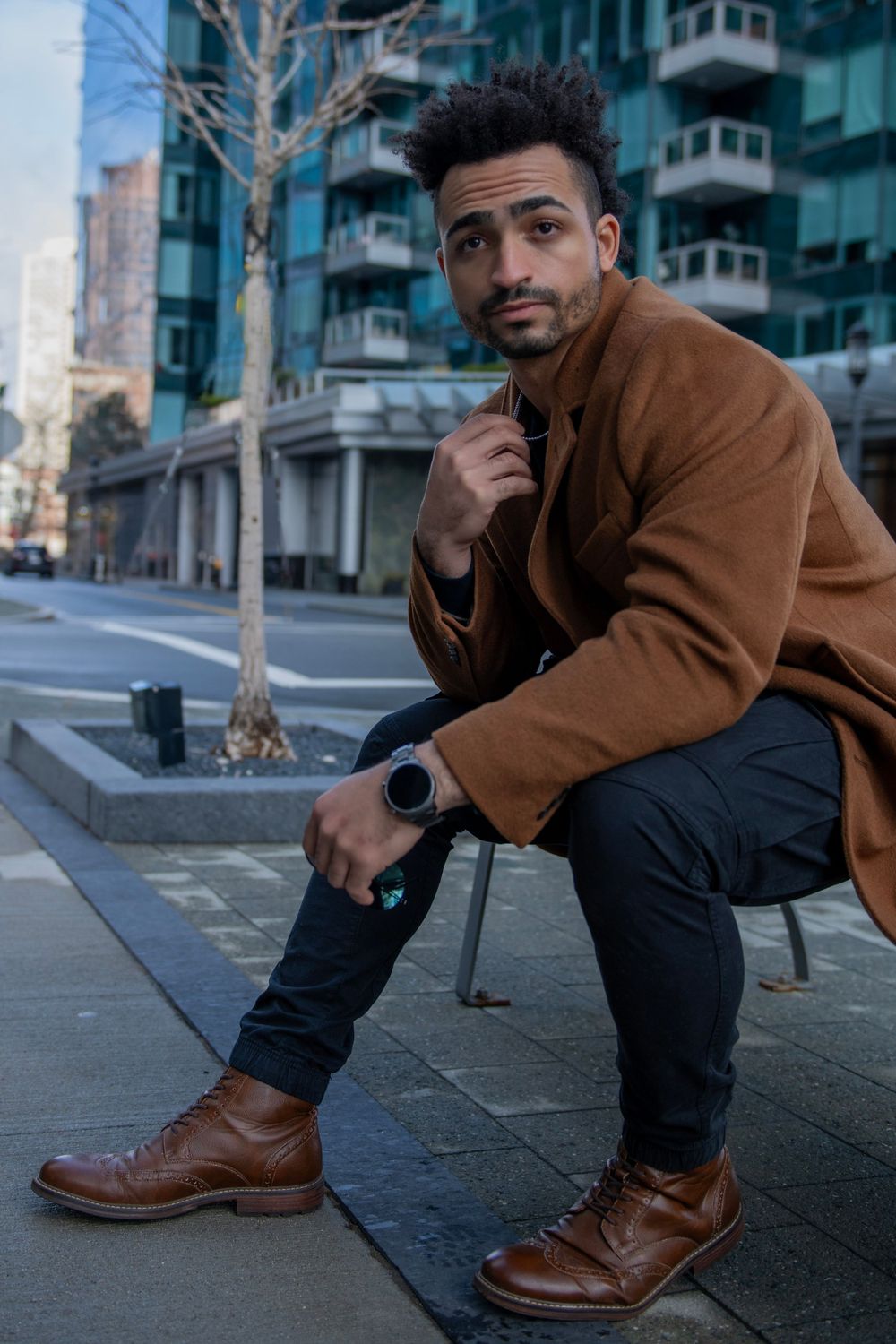 Urban fashion portrait with brown coat and leather boots on city sidewalk.