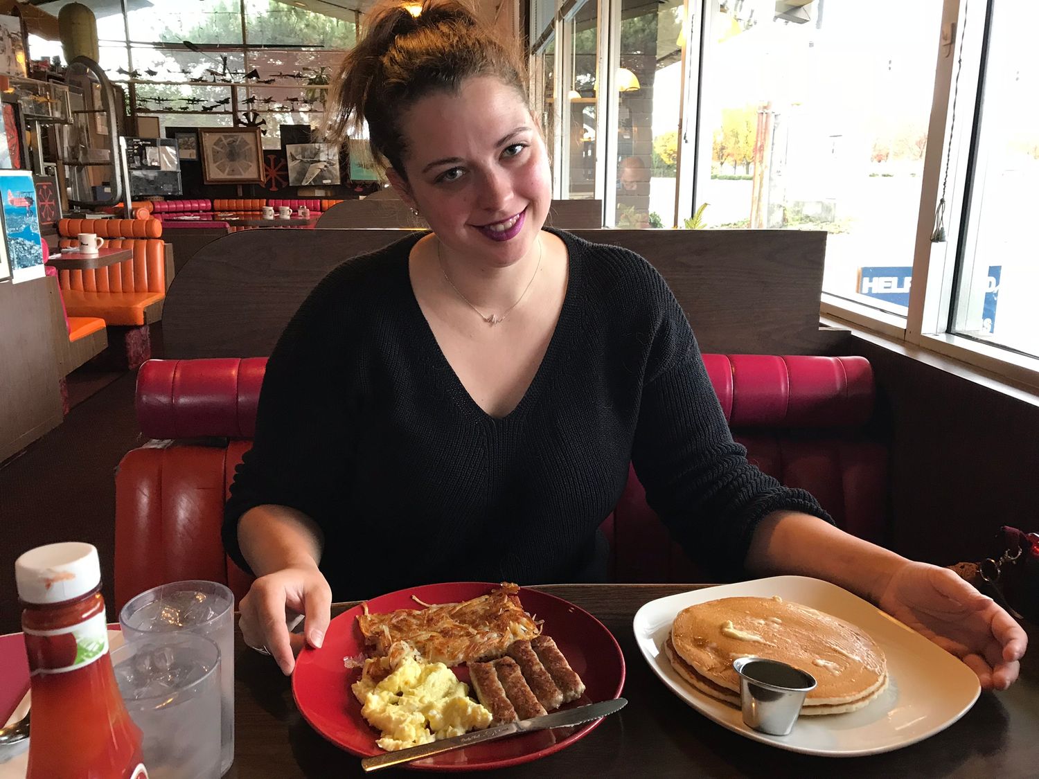 Restaurant patron with breakfast plate of eggs and pancakes at casual diner booth.