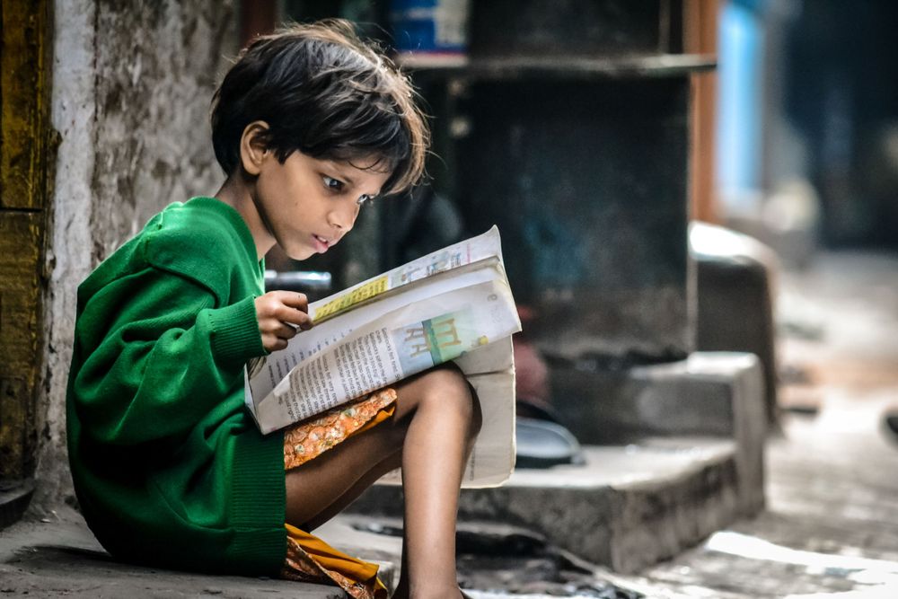 A child in a green sweater reads intently while sitting on stone steps outdoors.