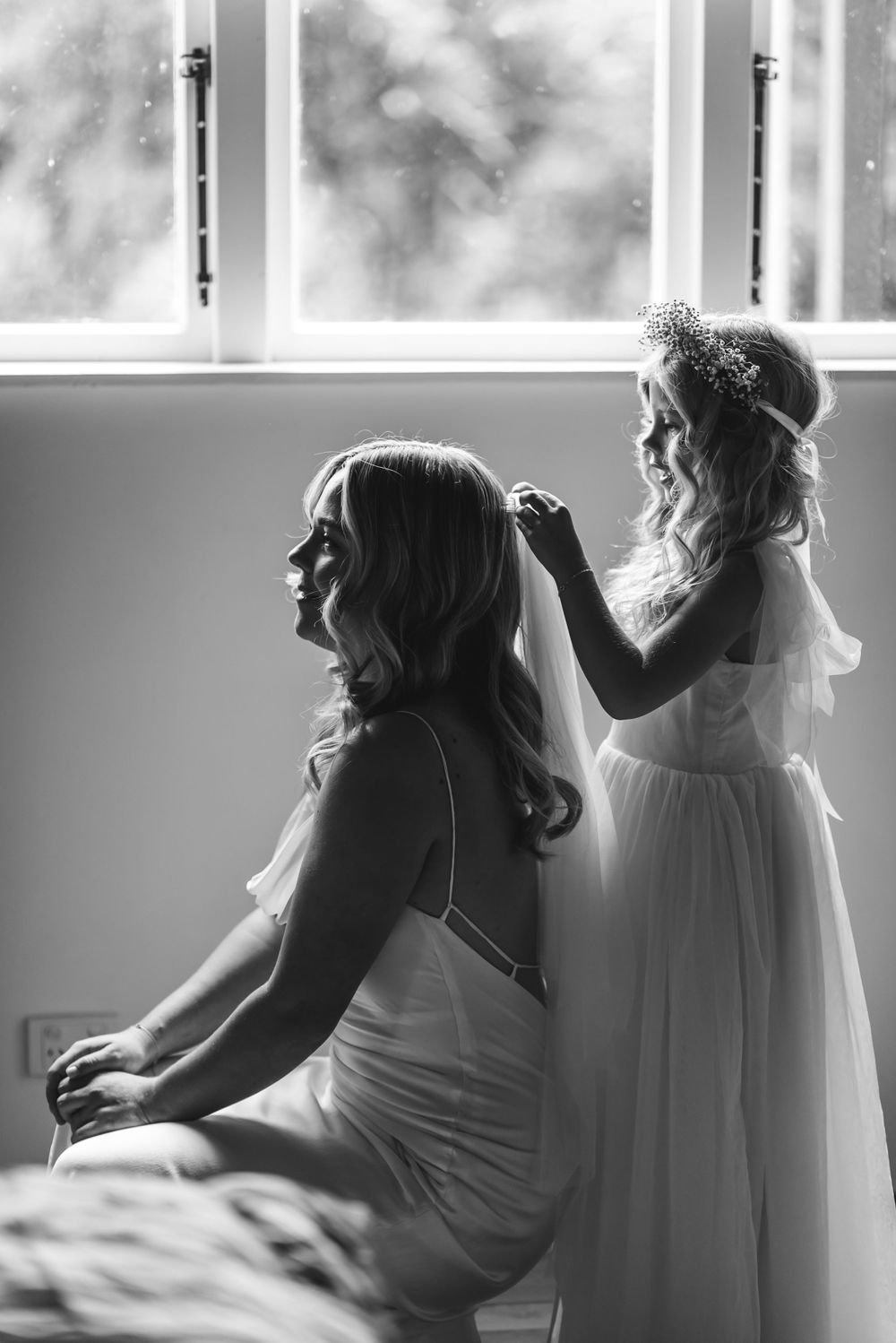 A touching black and white wedding preparation moment with a small figure adjusting a veil near a window.