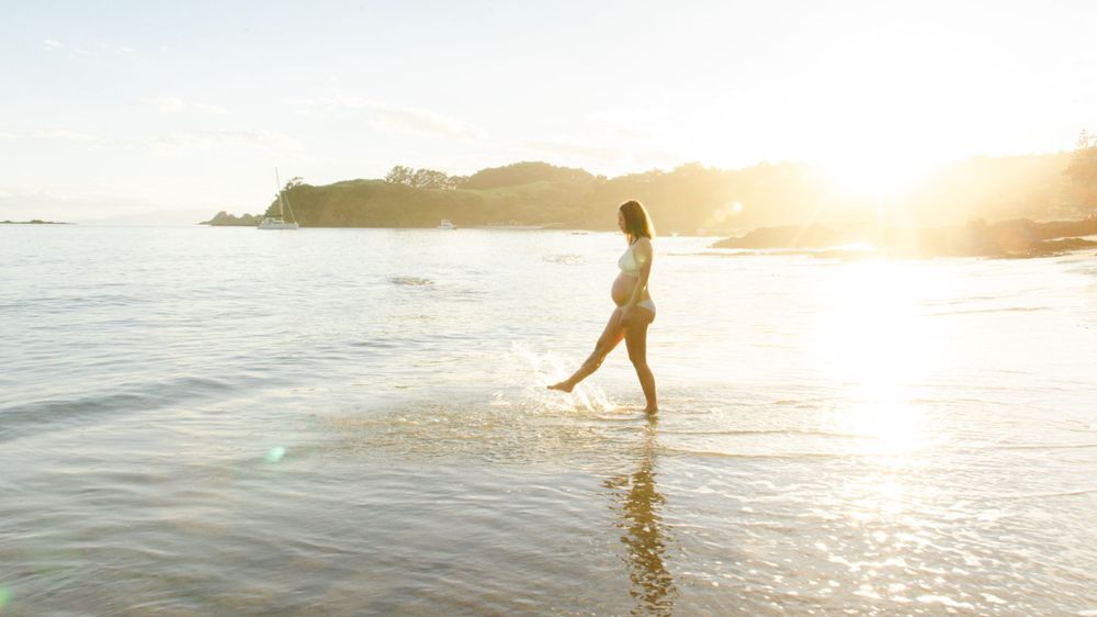 Silhouette of person walking along beach at sunset with golden light reflecting on wet sand.