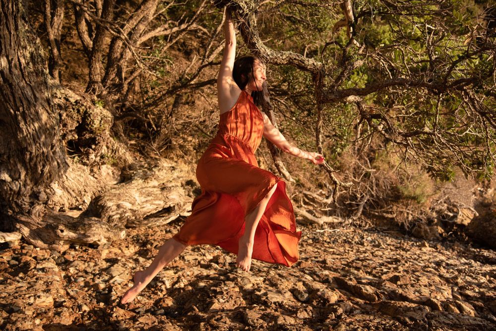 Woman in flowing red dress dancing among trees in natural sunlight.