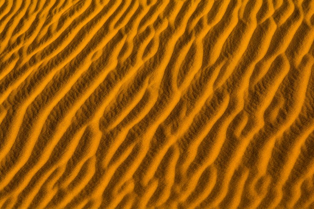 Abstract pattern of rippling orange sand dunes creating wavy lines and textures in desert landscape.