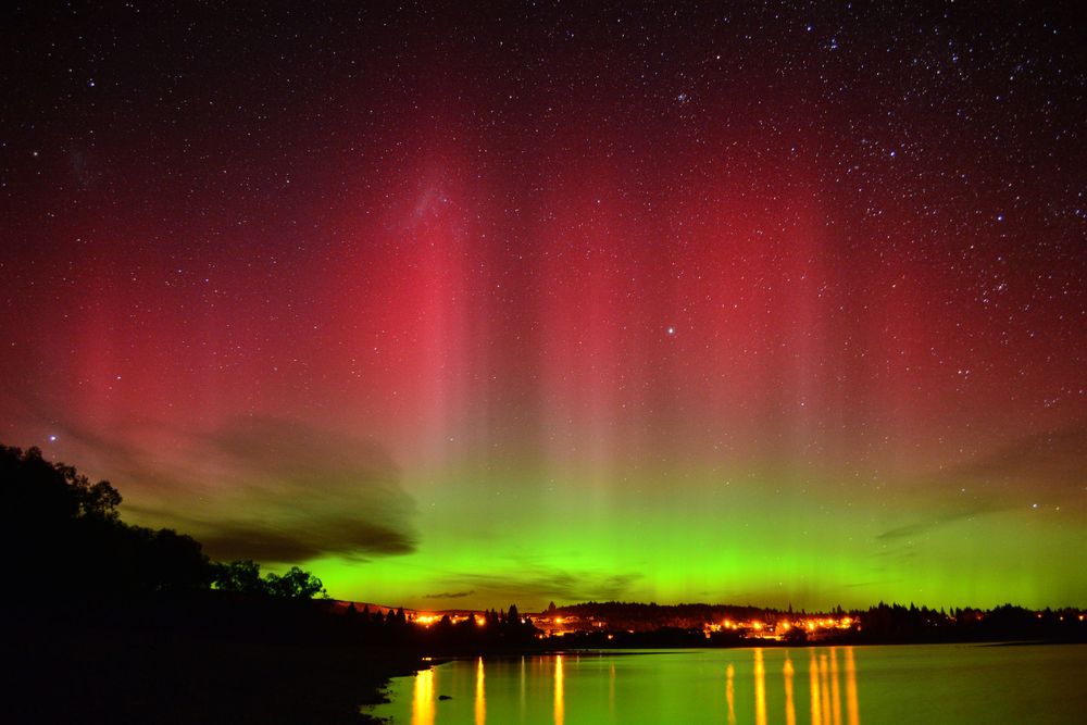 Vibrant red and green aurora borealis lights dance over a lake reflecting the colorful night sky.