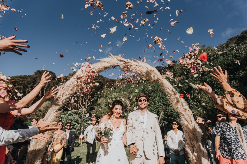 Wedding celebration with flower petals being thrown over couple under floral arch.