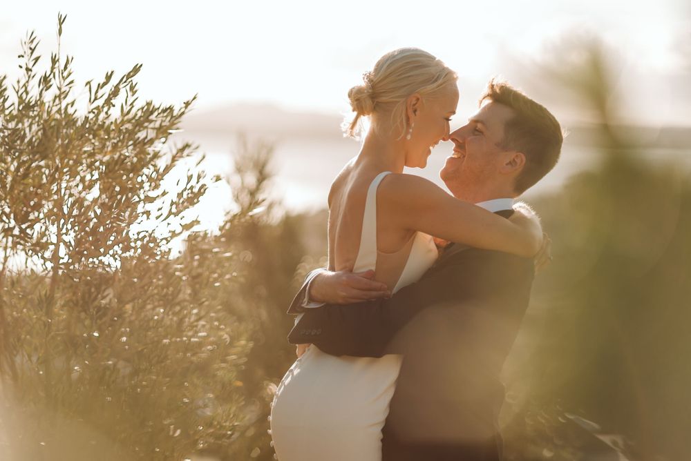 Romantic sunset silhouette of couple embracing in golden summer light among plants.