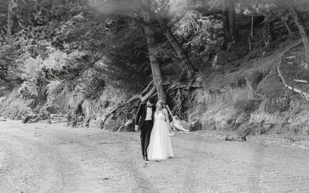 A black and white wedding photograph showing a couple standing on a country dirt road beside a rocky hillside.