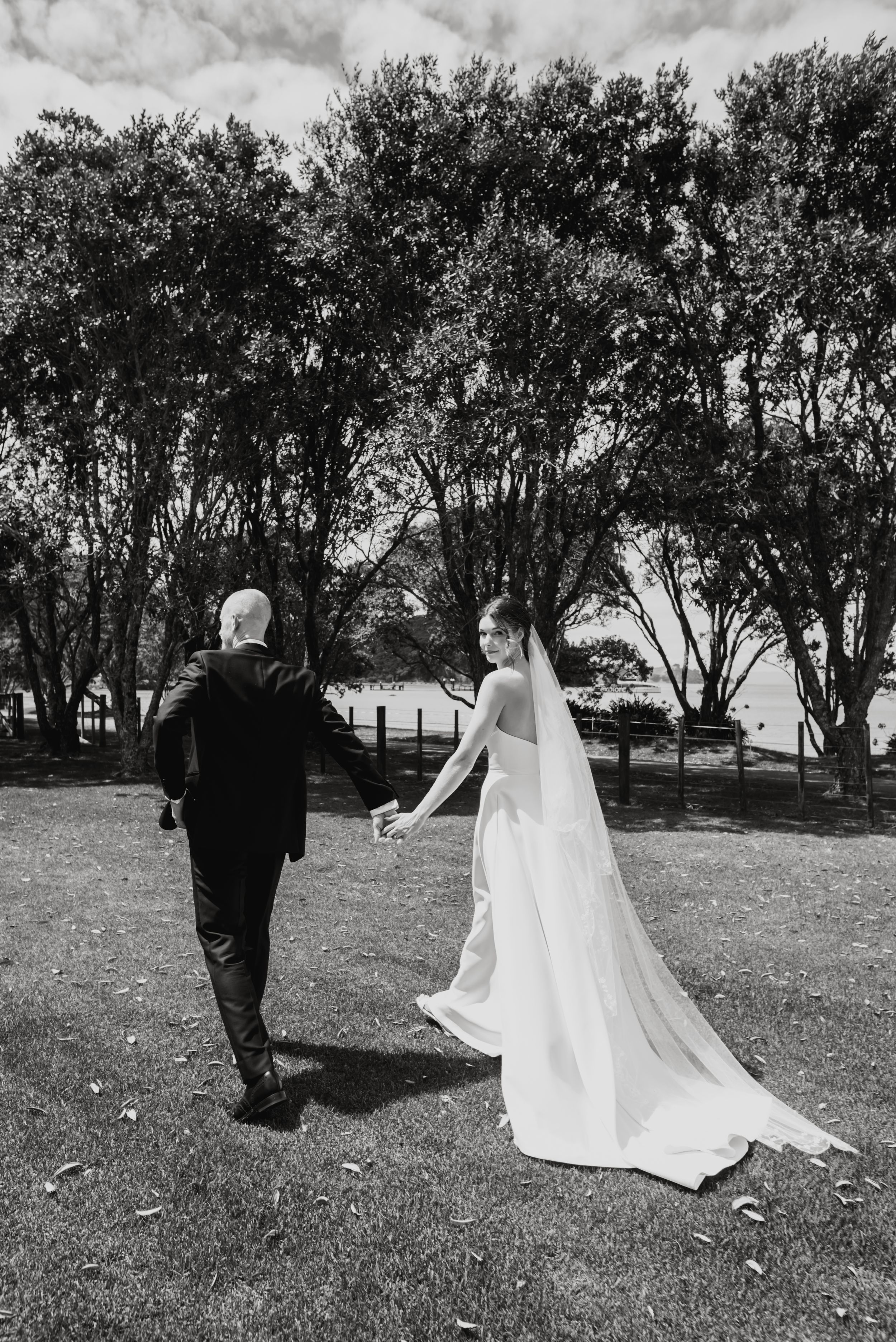 A black and white sequence of wedding photos showing a bride in flowing veil and groom walking across a grassy field.