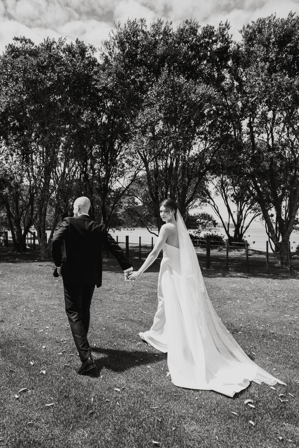 A black and white sequence of wedding photos showing a bride in flowing veil and groom walking across a grassy field.