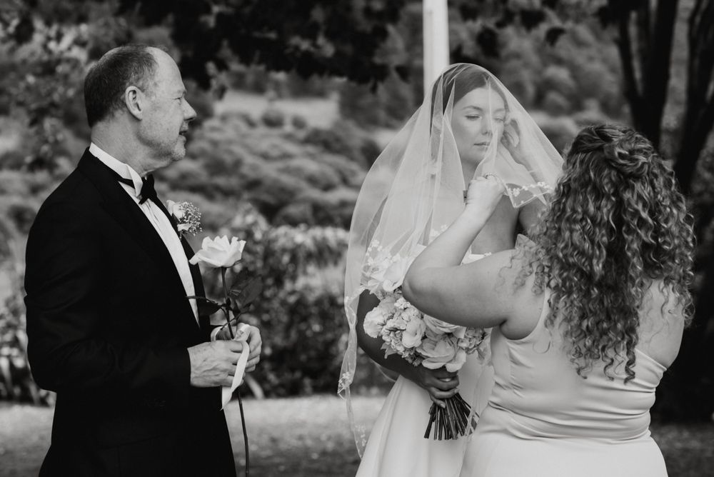 A candid black and white wedding photograph capturing a joyful emotional moment between people during an outdoor ceremony.