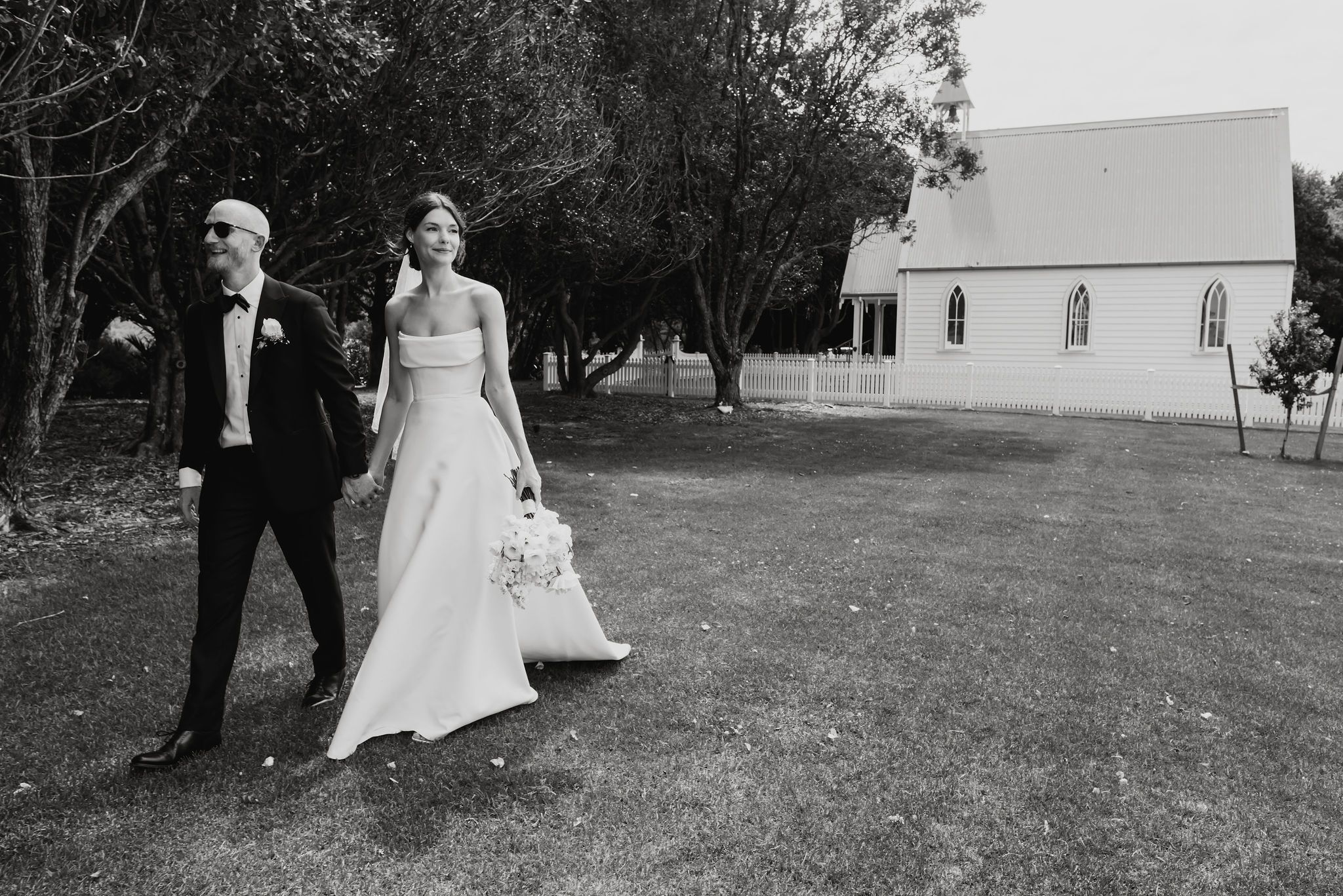 A black and white photograph of a couple walking outside a white country church on their wedding day.