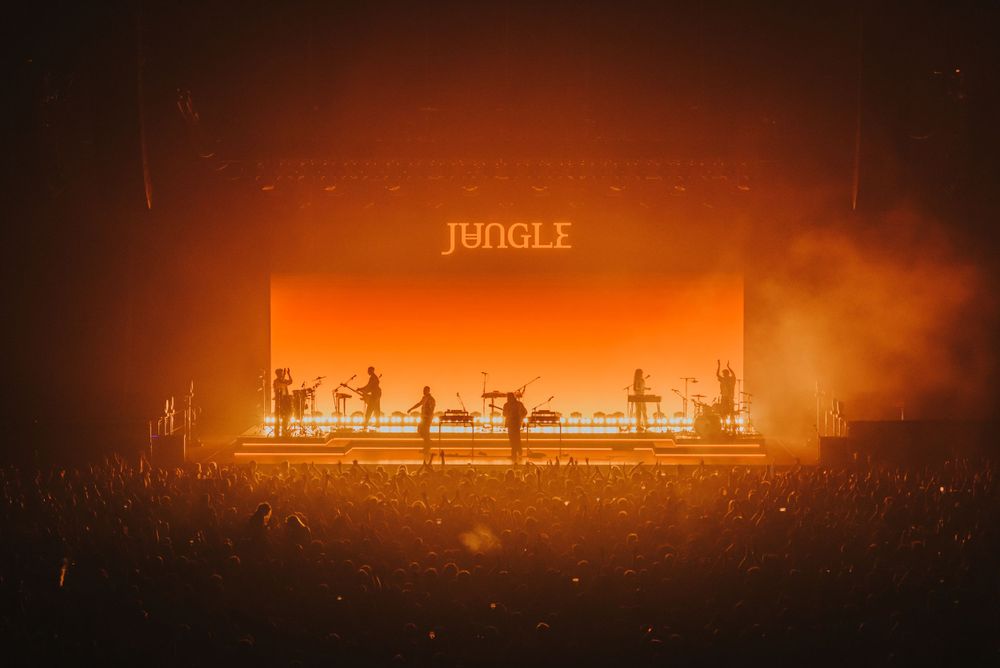 Concert stage lit with dramatic orange lighting displaying the word 'JUNGLE' against a smoky atmosphere.