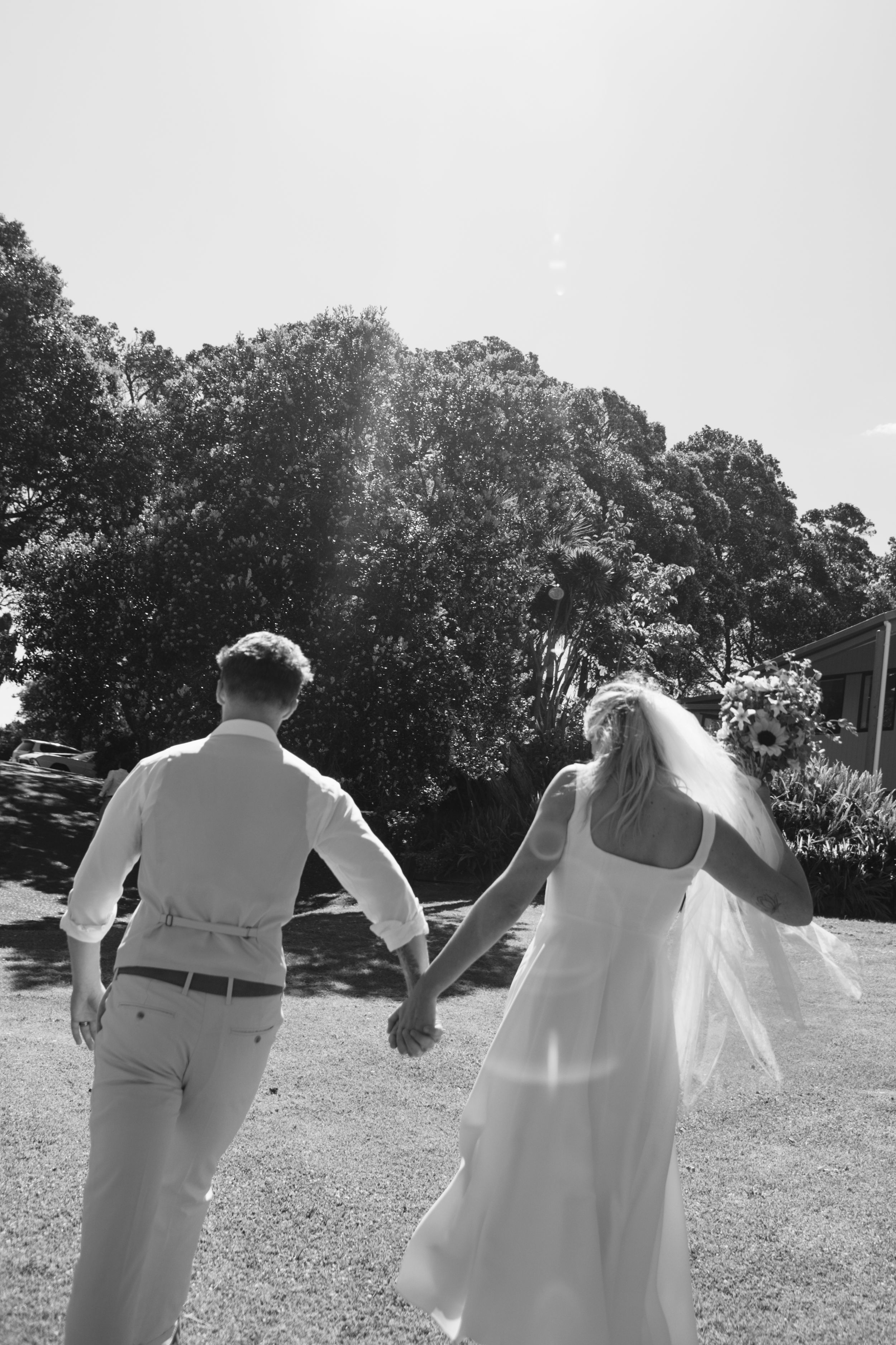 A couple in wedding attire walks through a sunny field while holding hands, shown in a series of candid shots.