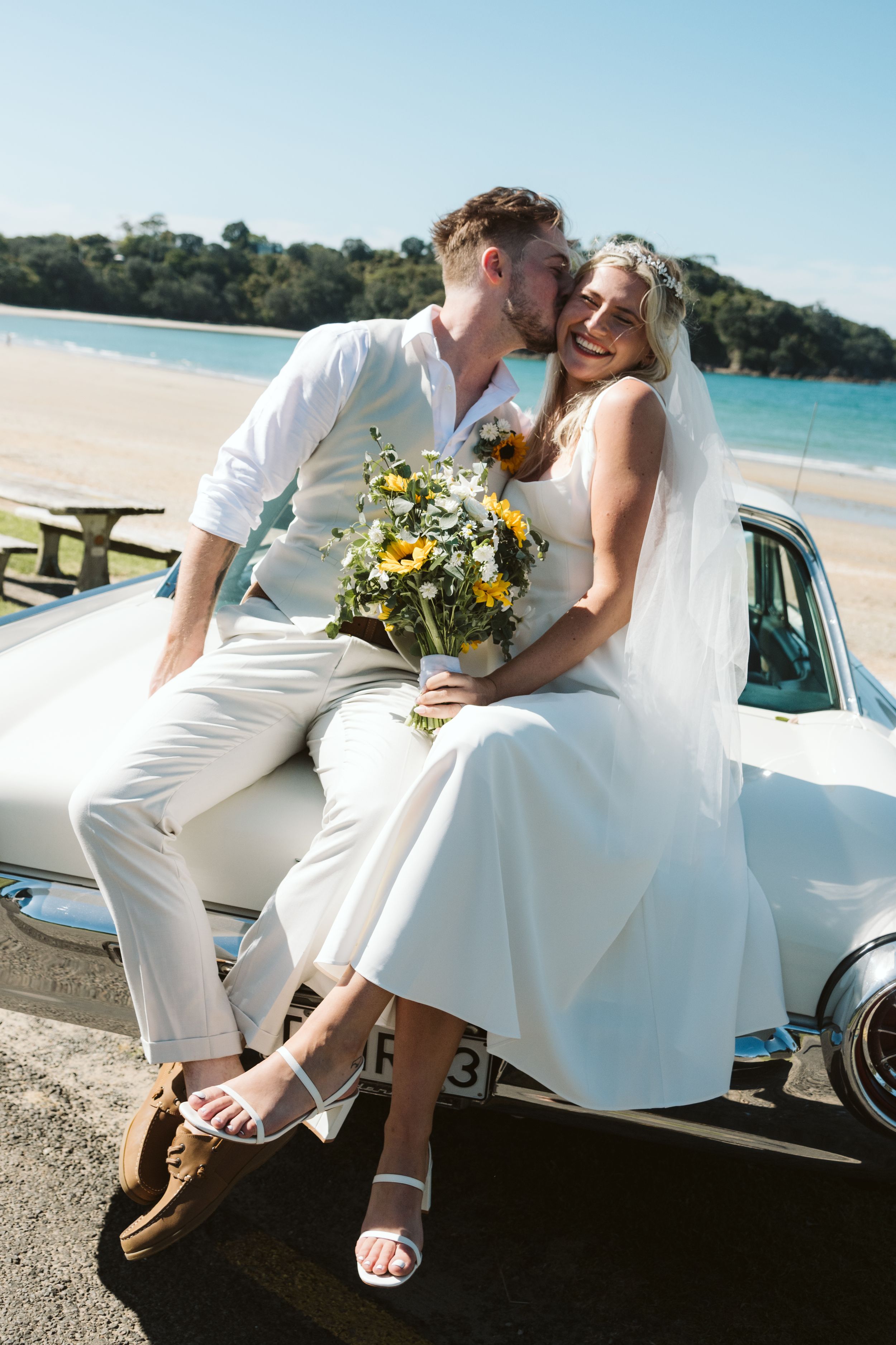 A romantic beach scene with a classic vintage car parked near the shoreline on a sunny day.