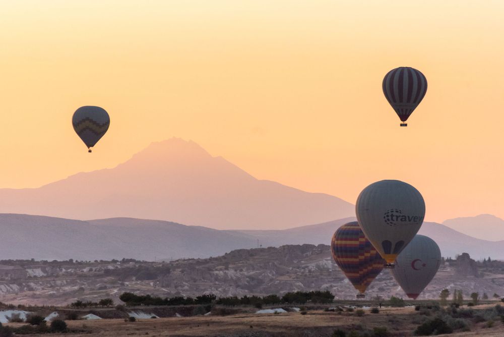 Hot air balloons drift across mountain landscape during golden sunset hour.