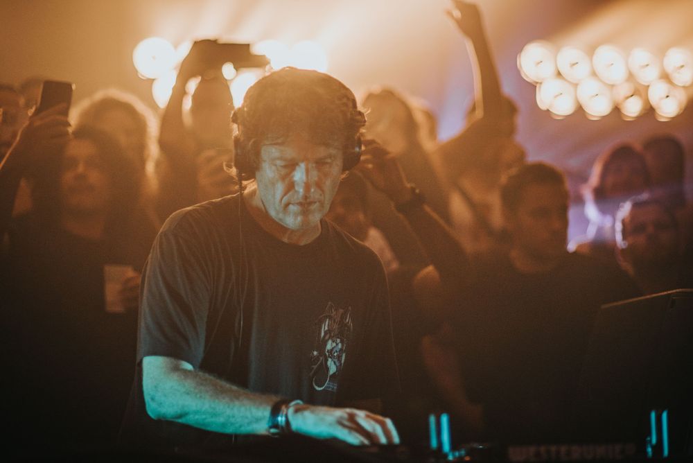 DJ performing at crowded nightclub with warm ambient lighting and energetic atmosphere.