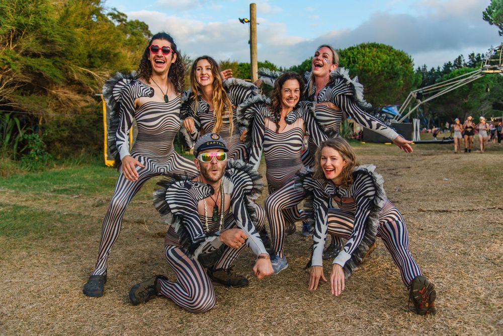 A group in matching striped costumes poses playfully outdoors during a performance or event.