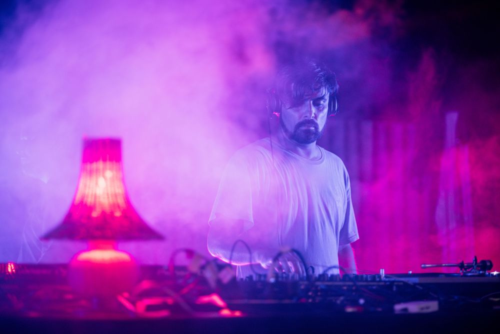 DJ performing in purple haze with red lamp creating atmospheric lighting effects.