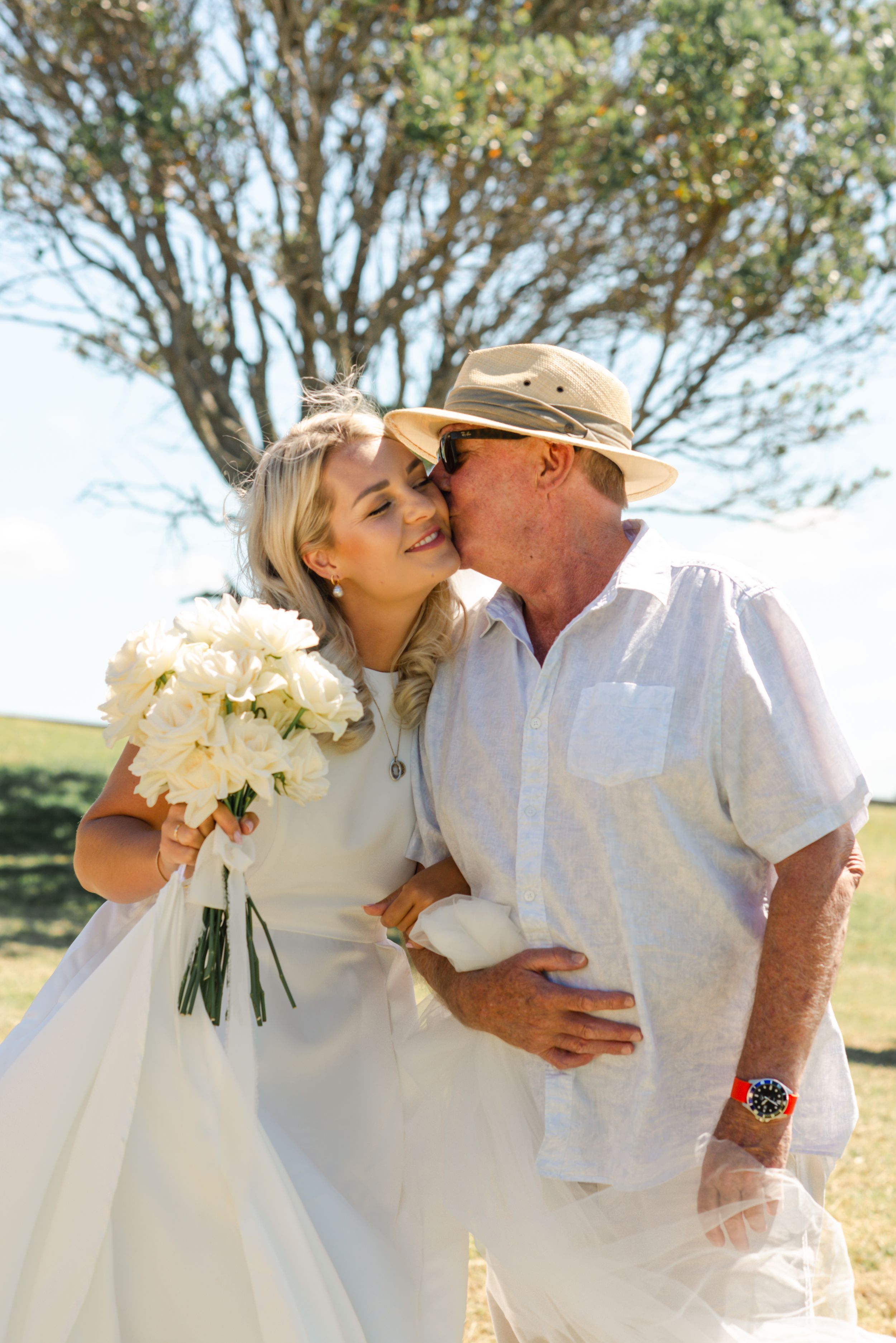 A romantic outdoor wedding moment with a bouquet of white flowers and trees in the background on a sunny day.