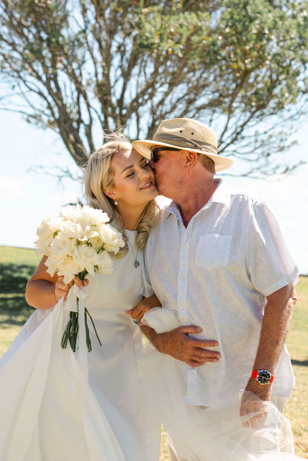 A romantic outdoor wedding moment with a bouquet of white flowers and trees in the background on a sunny day.