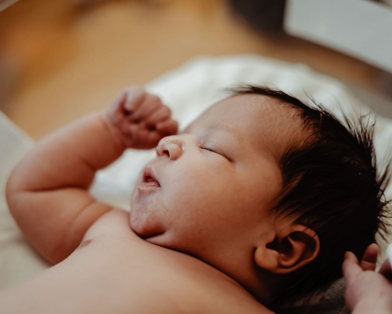 Sleeping newborn baby with dark hair lying peacefully on white blanket.