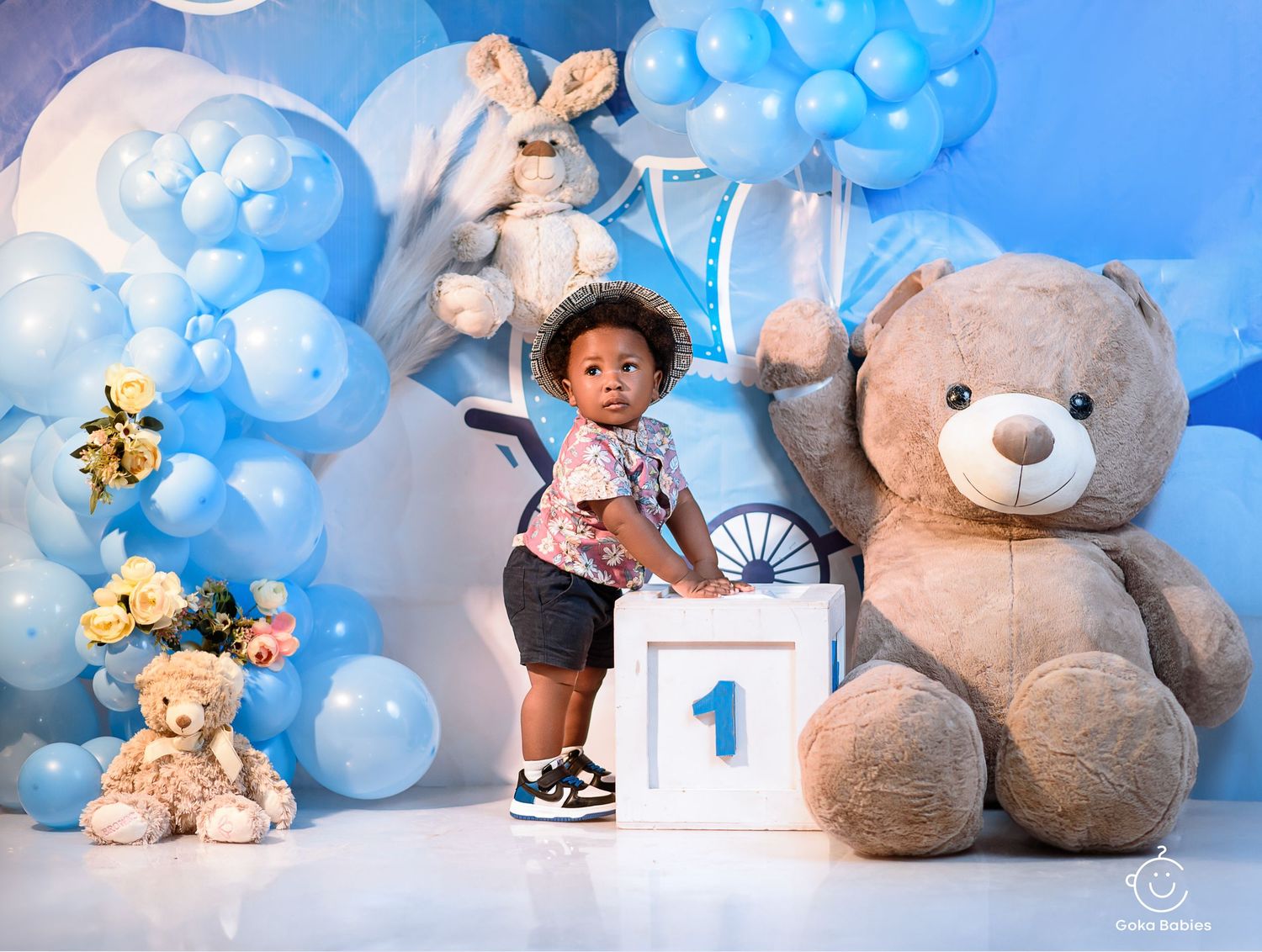 First birthday celebration setup with blue balloons and large teddy bear decorations.