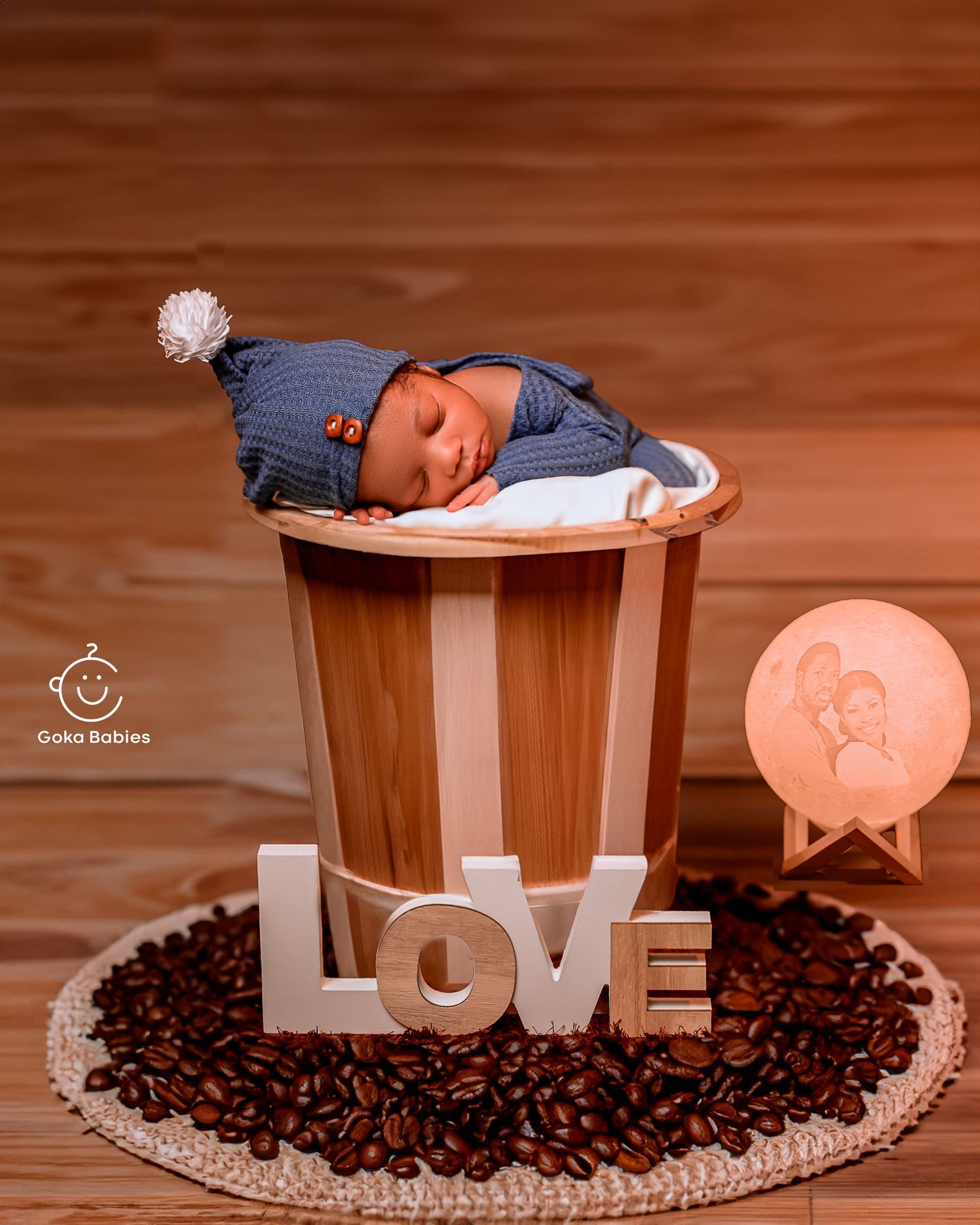 A sleeping baby in blue attire on a wooden surface with coffee beans and LOVE letters decoration.