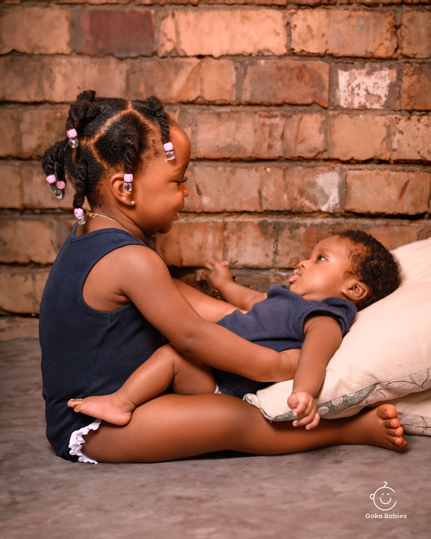 Two young people sharing a tender moment on the floor against a rustic brick wall background.