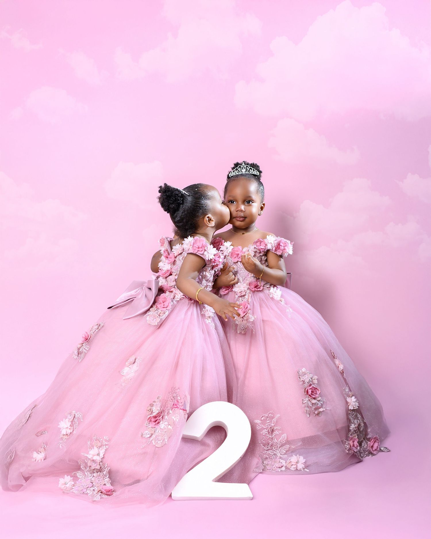 Two dancers in pink floral tulle dresses pose gracefully against a soft pink backdrop with a decorative number 2.