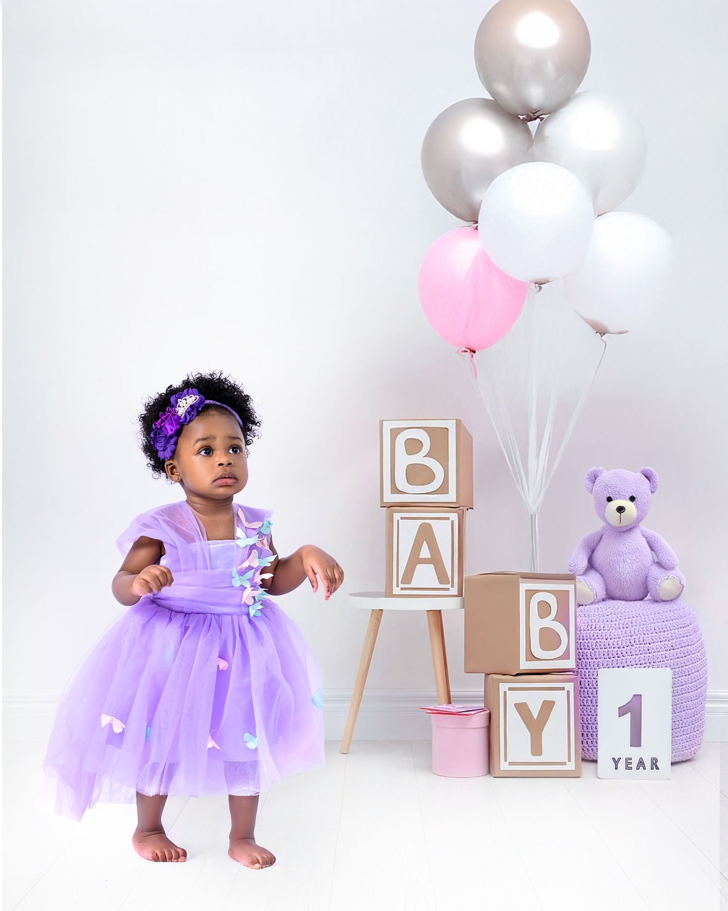Purple tulle dress and party decor with silver balloons, blocks spelling 'BABY', and lavender teddy bear for first birthday.