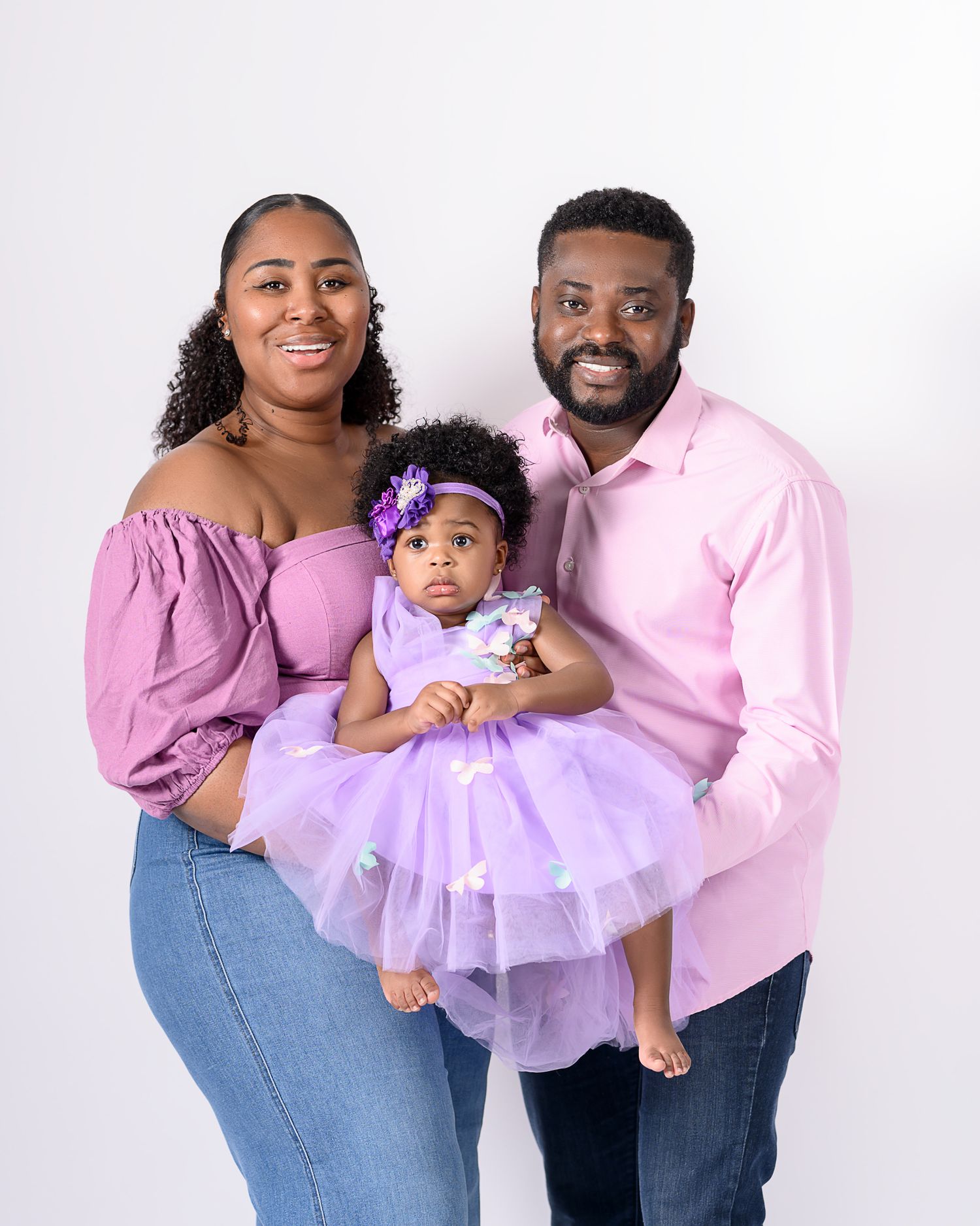 A family in coordinating pink outfits poses together against a white backdrop for a studio portrait.