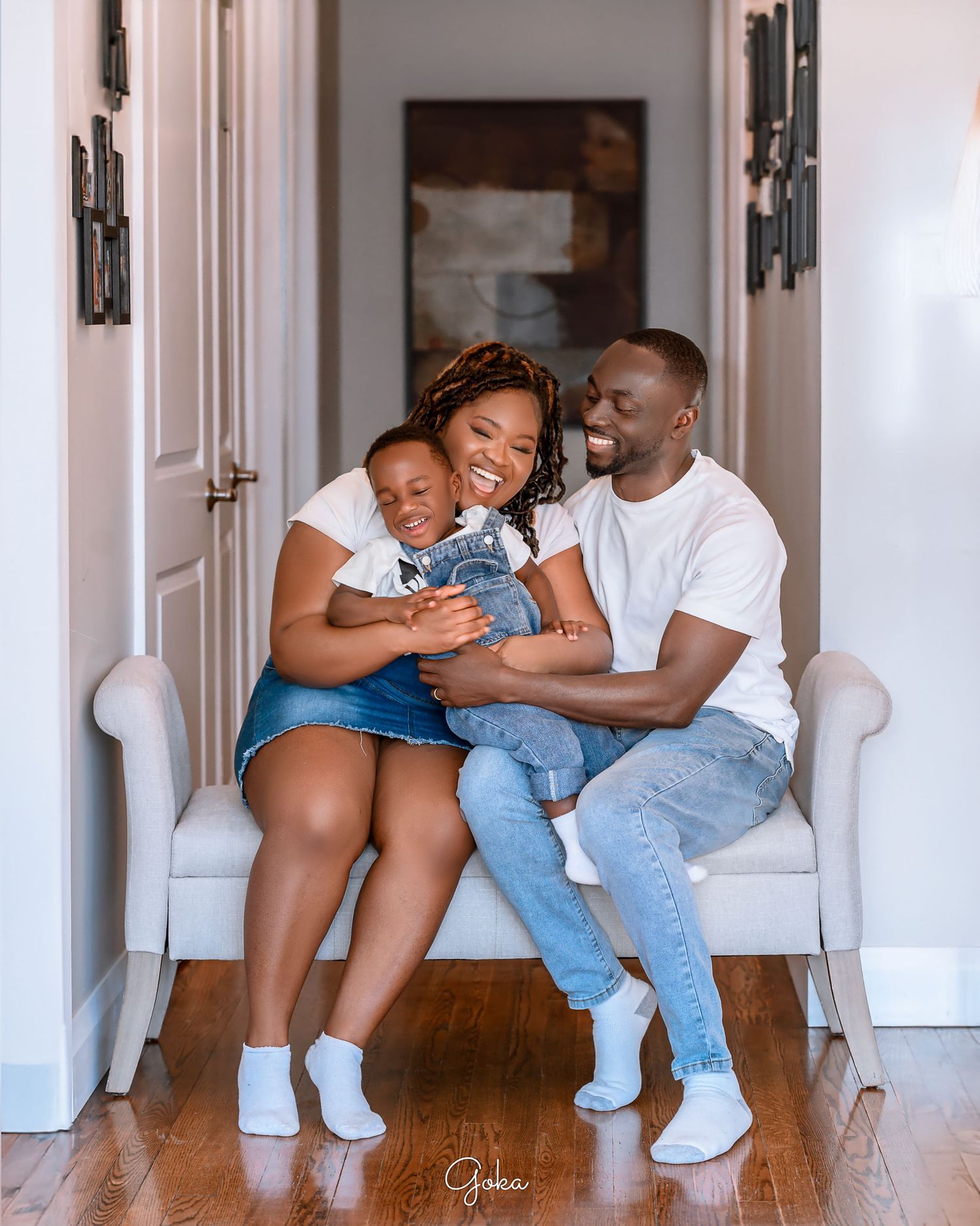 Family of three sharing joyful moment together on white bench in hallway.