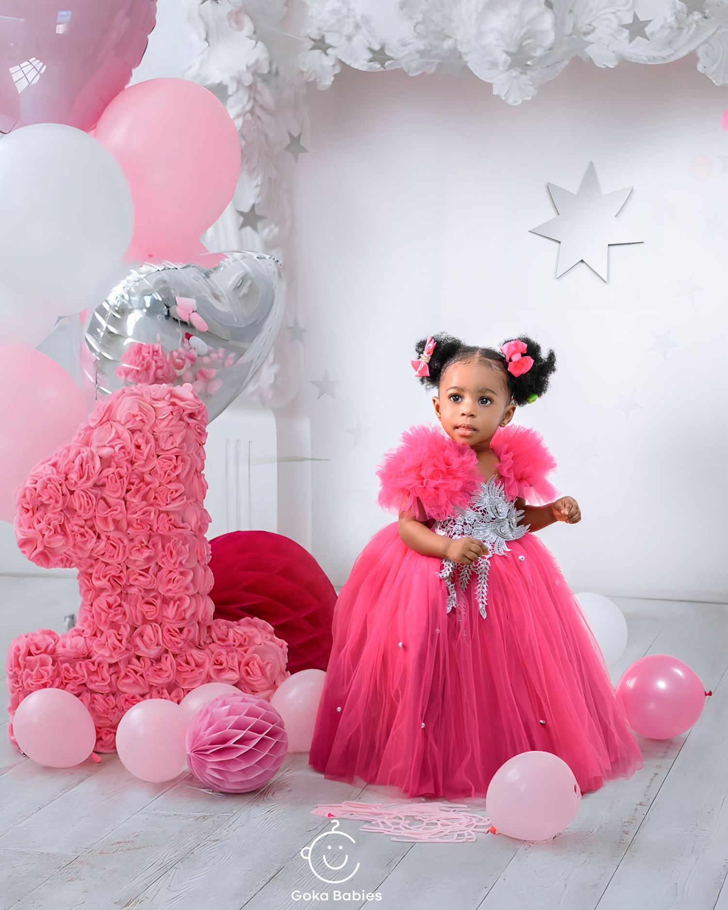 Pink tulle princess gown sparkles beside decorative number one at first birthday celebration.