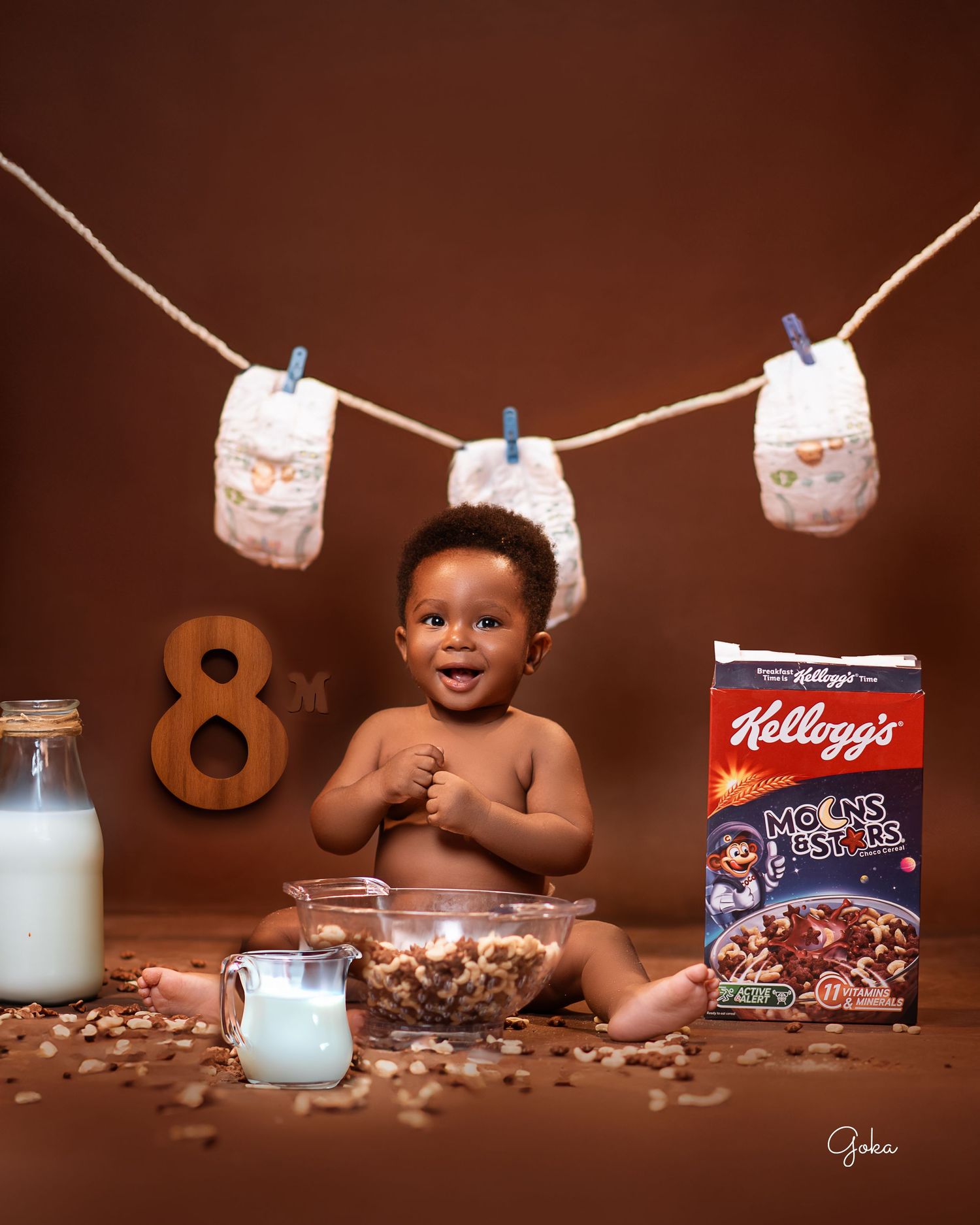 Joyful breakfast-themed photo with cereal, milk, and hanging diapers against brown backdrop.