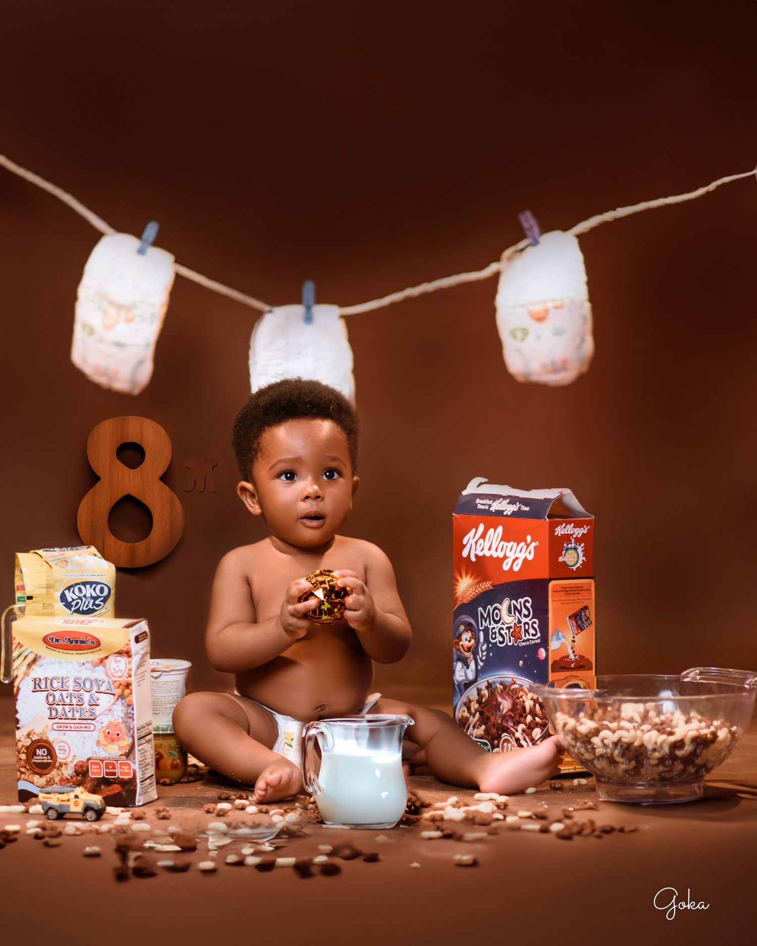 Creative milk and cereal themed photo setup with diapers hanging on string and cereal boxes.