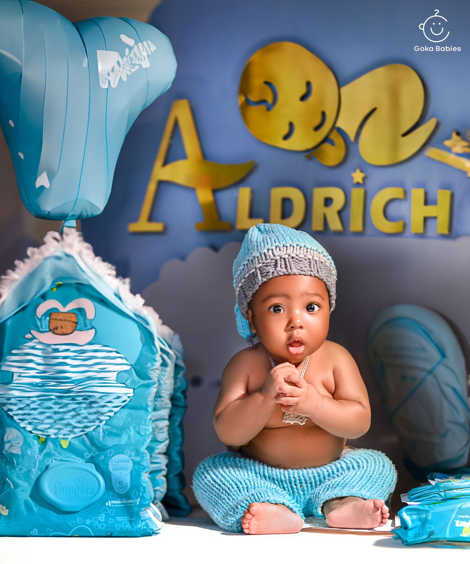 A baby in blue attire sits against a blue backdrop with decorative elements and text.