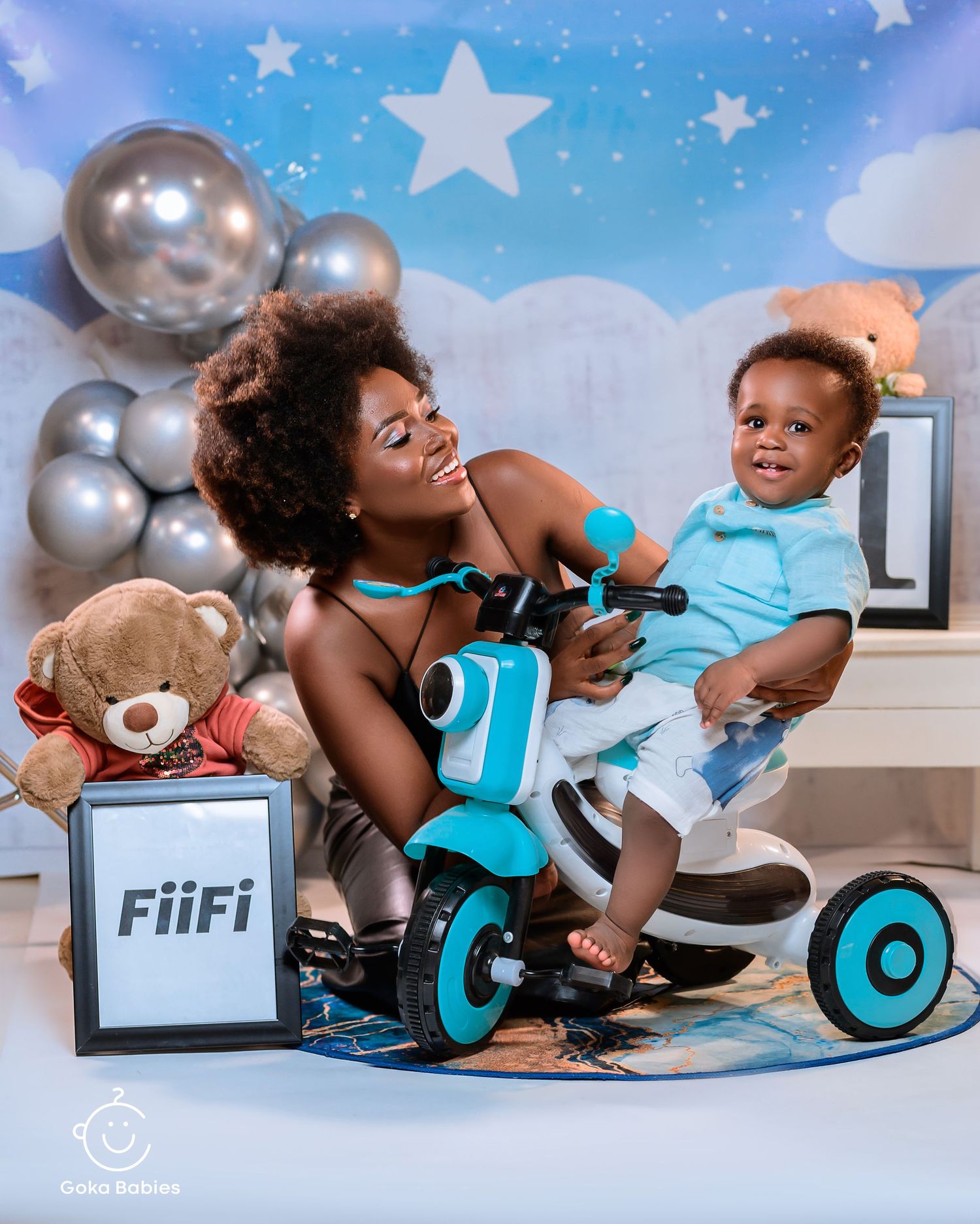 Birthday photoshoot with turquoise tricycle and silver balloon decorations.