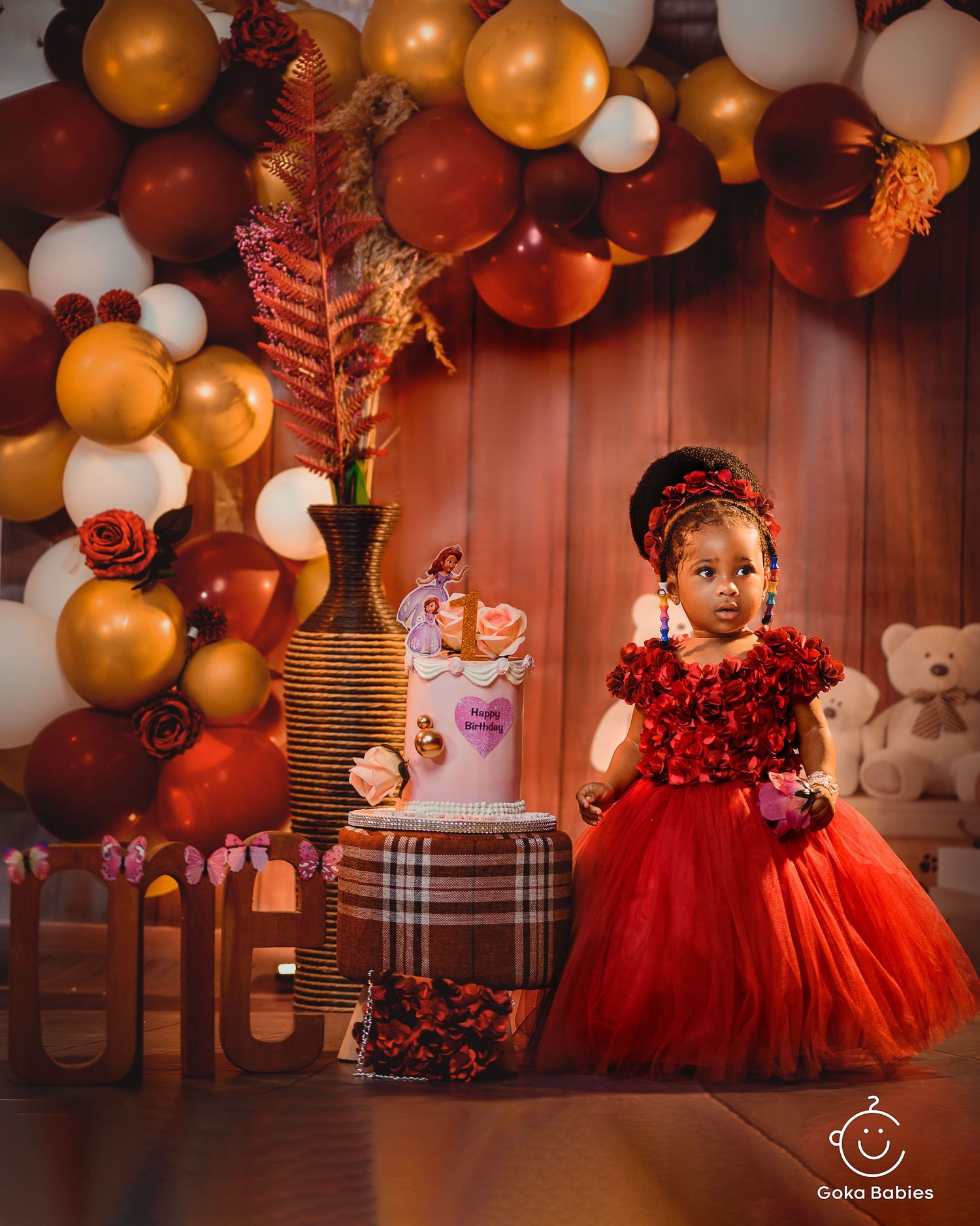 Sparkling red ball gown stands out against elegant balloon arch and party decorations.