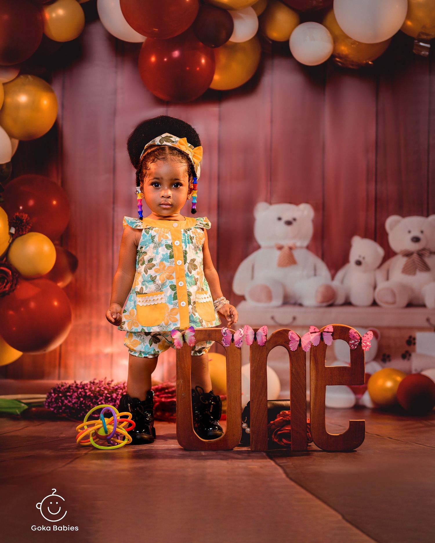 Yellow floral dress and black boots complement balloon arch and teddy bear decorations.