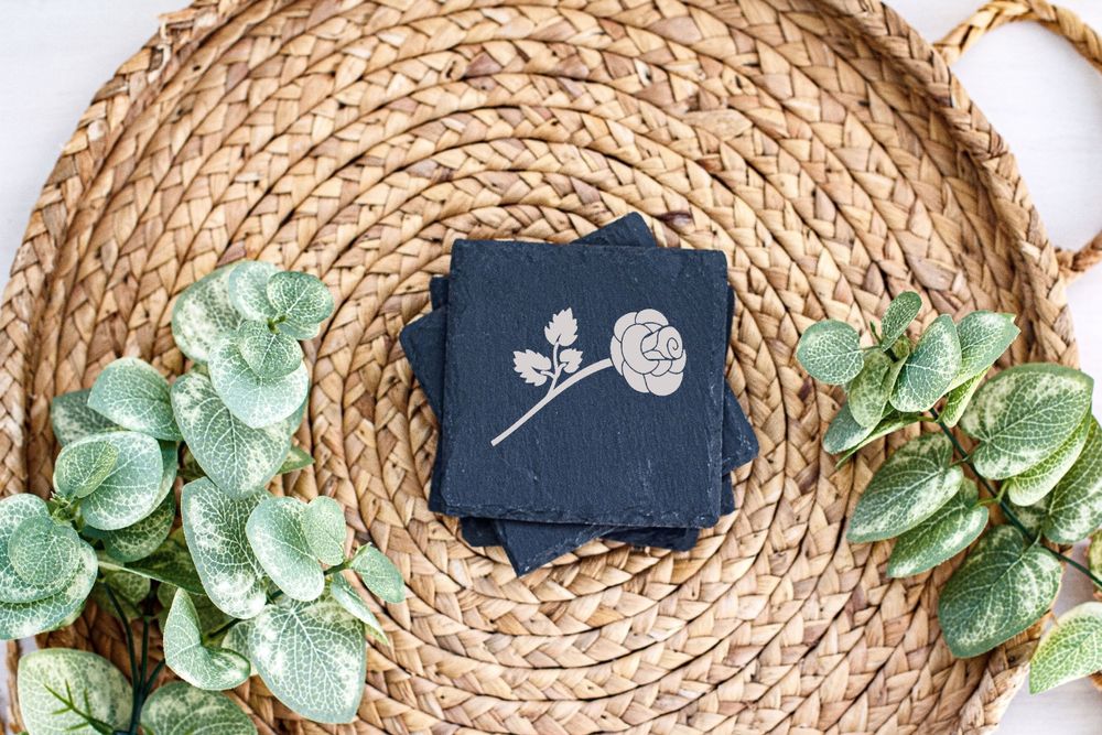 Single rose illustration on navy card displayed on woven rattan mat with green leaf accents.