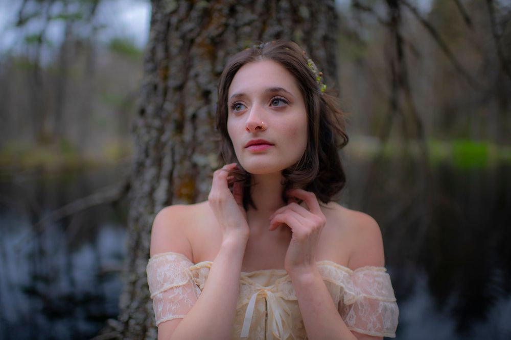 Dreamy portrait of woman in vintage lace dress against moody forest backdrop.