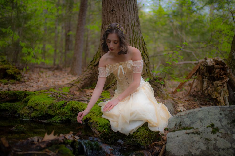 Whimsical forest scene with cream-colored vintage dress against mossy rocks and trees.