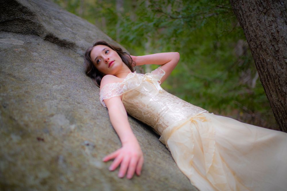 Dreamy portrait on stone featuring cream vintage dress in natural woodland setting.