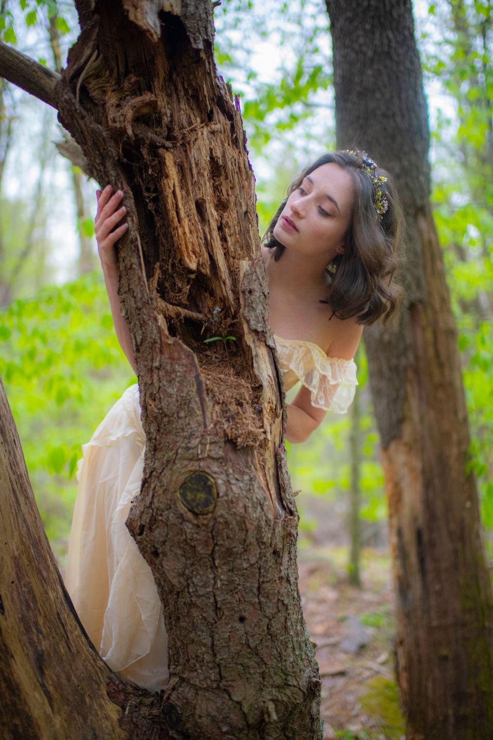 Artistic forest portrait with vintage dress and weathered tree trunk creating a fairytale atmosphere.