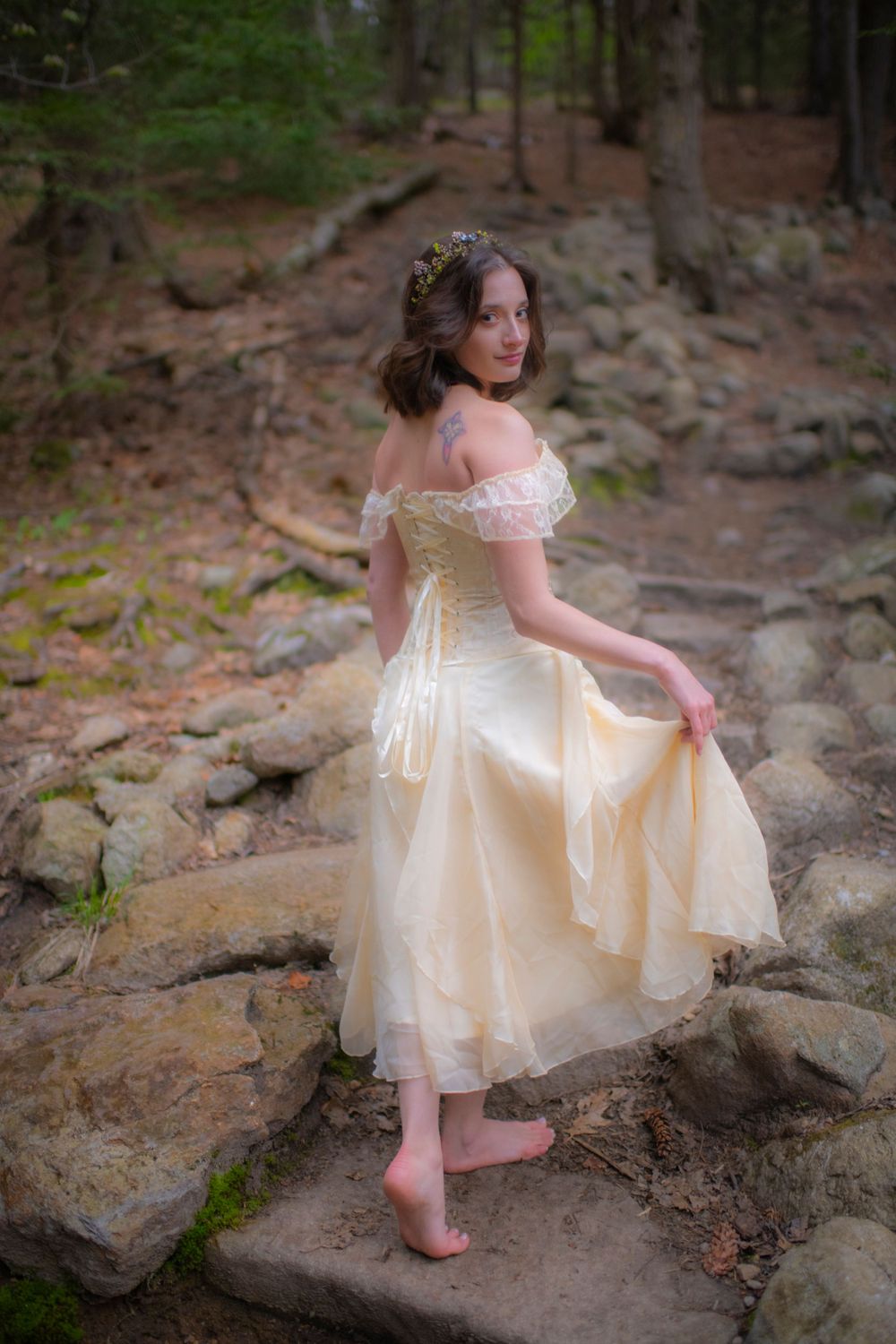 Barefoot dancer in vintage cream dress poses gracefully on forest rocks.
