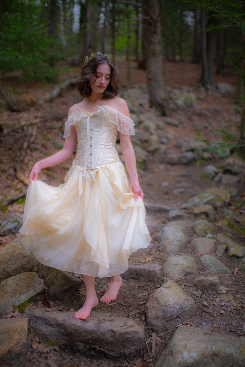 Ethereal woodland scene with vintage corset dress and barefoot steps on rocky path.