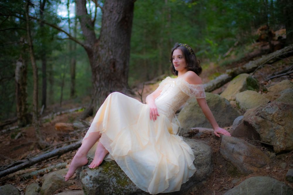 Romantic forest portrait with flowing cream dress against rocky woodland backdrop.
