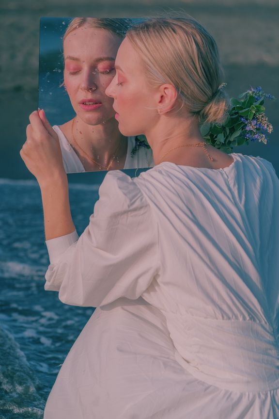 A woman in a white dress holding a mirror