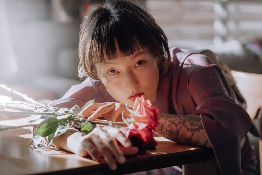 A Japanese woman wearing a kimono, resting her arm and head on a table adorned with roses
