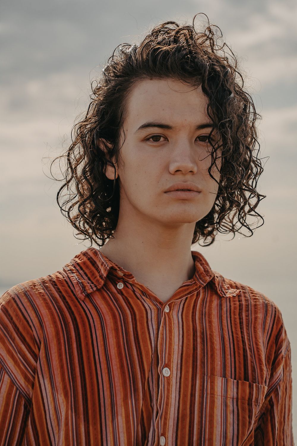 Portrait of a curly-haired man in an orange-striped shirt